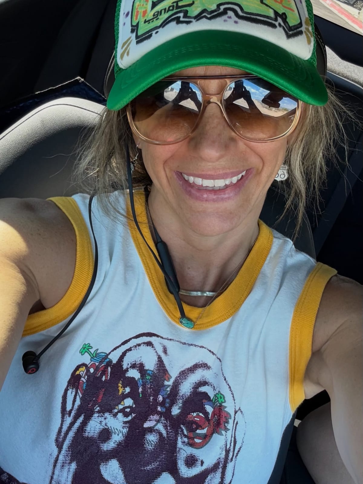 Samantha smiling in sunglasses, a green trucker cap and a graphic tank top